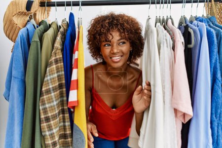 Photo for Young african american woman smiling confident appearing through rack at clothing store - Royalty Free Image