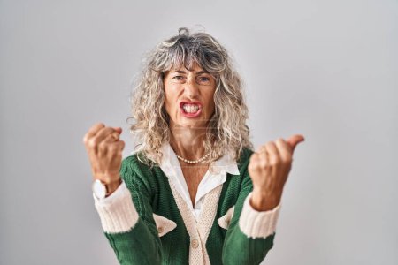 Téléchargez les photos : Middle age woman standing over white background angry and mad raising fists frustrated and furious while shouting with anger. rage and aggressive concept. - en image libre de droit