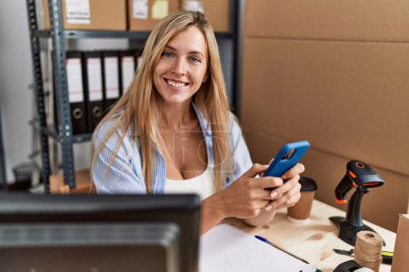 Téléchargez les photos : Jeune femme blonde ecommerce travailleur d'affaires en utilisant smartphone au bureau - en image libre de droit