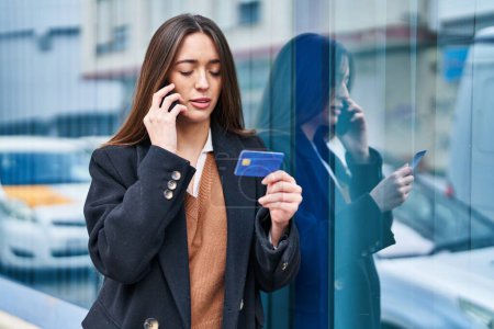 Téléchargez les photos : Jeune belle femme hispanique parlant sur smartphone tenant la carte de crédit à la rue - en image libre de droit