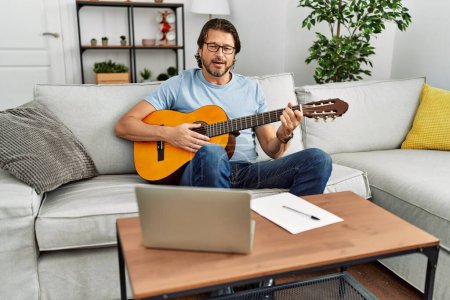 Photo for Middle age caucasian man playing classical guitar at home - Royalty Free Image