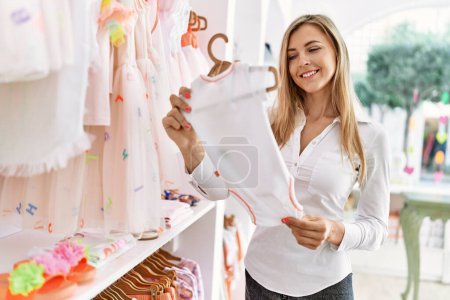 Téléchargez les photos : Jeune cliente caucasienne souriante heureuse de choisir des vêtements de bébé au magasin de vêtements. - en image libre de droit