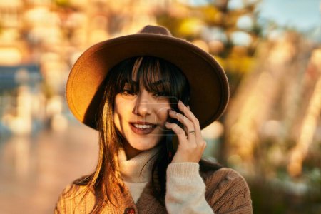 Photo for Brunette woman wearing winter hat smiling speaking on the phone at the park - Royalty Free Image