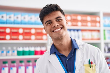 Foto de Joven farmacéutico hispano sonriendo confiado de pie en la farmacia - Imagen libre de derechos