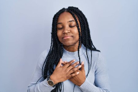 Photo for African american woman standing over blue background smiling with hands on chest with closed eyes and grateful gesture on face. health concept. - Royalty Free Image
