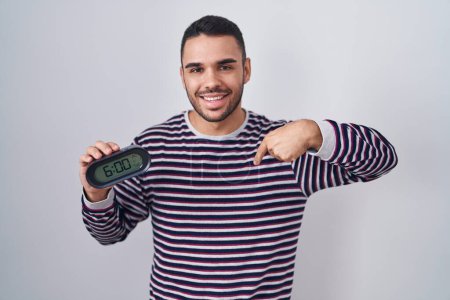 Photo for Young hispanic man wearing pyjama holding alarm clock pointing finger to one self smiling happy and proud - Royalty Free Image