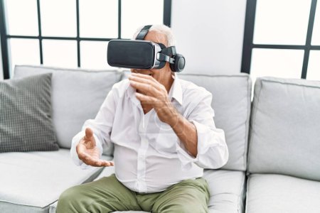 Téléchargez les photos : Homme âgé jouant à un jeu vidéo en utilisant des lunettes de réalité virtuelle à la maison - en image libre de droit