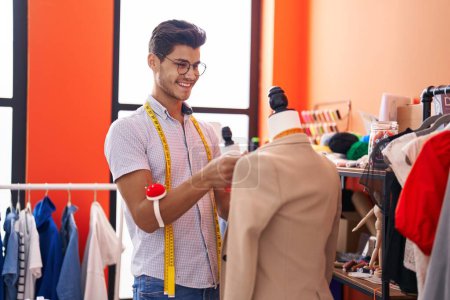Téléchargez les photos : Young hispanic man tailor smiling confident measuring t shirt at atelier - en image libre de droit