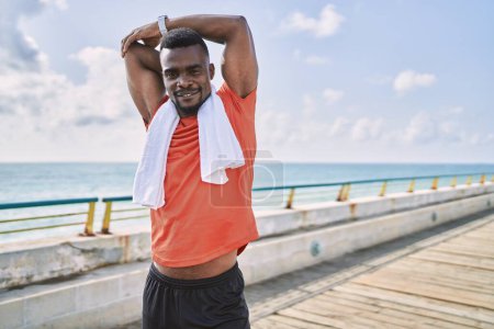 Foto de Young african american man wearing sportswear stretching at seaside - Imagen libre de derechos