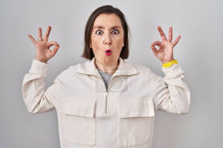 Photo for Middle age hispanic woman standing over isolated background looking surprised and shocked doing ok approval symbol with fingers. crazy expression - Royalty Free Image