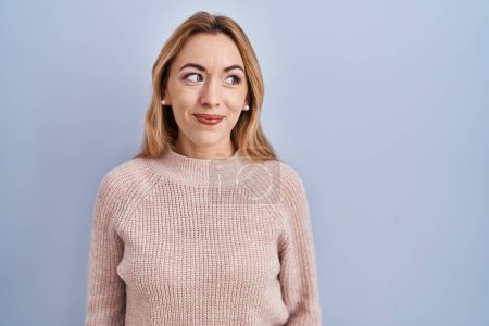 Photo for Hispanic woman standing over blue background smiling looking to the side and staring away thinking. - Royalty Free Image