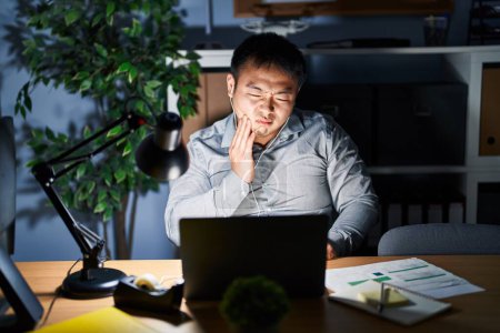 Foto de Young chinese man working using computer laptop at night touching mouth with hand with painful expression because of toothache or dental illness on teeth. dentist - Imagen libre de derechos