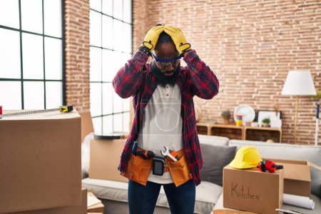 Foto de African american man working at home renovation suffering from headache desperate and stressed because pain and migraine. hands on head. - Imagen libre de derechos