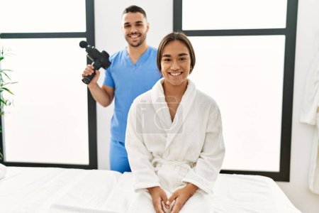 Téléchargez les photos : Latin homme et femme portant uniforme de physiothérapie tenant pistolet à percussion en attente de massage au centre de beauté - en image libre de droit
