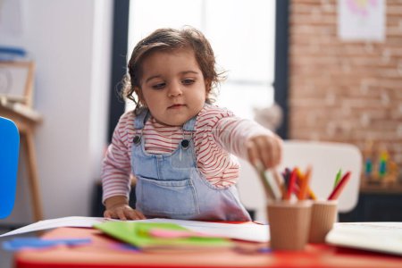 Foto de Adorable estudiante hispana sentada en la mesa dibujando sobre papel en el jardín de infantes - Imagen libre de derechos