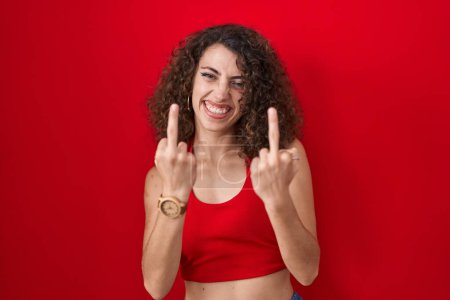 Photo for Hispanic woman with curly hair standing over red background showing middle finger doing fuck you bad expression, provocation and rude attitude. screaming excited - Royalty Free Image