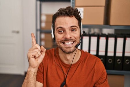 Foto de Joven hombre hispano usando auriculares de agente de centro de llamadas sonriendo feliz señalando con la mano y el dedo hacia un lado - Imagen libre de derechos