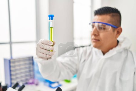 Photo for Young latin man scientist wearing covid protection uniform holding test tubes at laboratory - Royalty Free Image