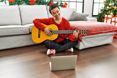 Photo for Hispanic woman with short hair learning classical guitar from online tutorial looking positive and happy standing and smiling with a confident smile showing teeth - Royalty Free Image