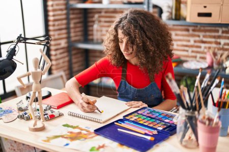 Photo for Young hispanic woman artist drawing on notebook at art studio - Royalty Free Image