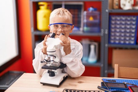 Foto de Adorable toddler student using microscope standing at classroom - Imagen libre de derechos