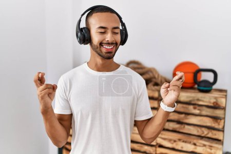 Photo for African american man listening to music using headphones at the gym gesturing finger crossed smiling with hope and eyes closed. luck and superstitious concept. - Royalty Free Image