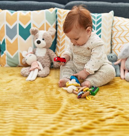 Téléchargez les photos : Adorable rousse tout-petit jouant avec jouet de voiture assis sur le canapé à la maison - en image libre de droit
