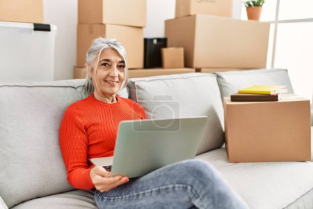 Photo for Middle age grey-haired woman smiling confident using laptop at new home - Royalty Free Image