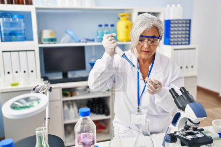 Téléchargez les photos : Femme d'âge moyen portant un uniforme de scientifique travaillant au laboratoire - en image libre de droit