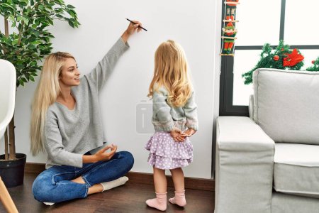 Téléchargez les photos : Mère et fille mesurant la hauteur de l'enfant marque d'écriture sur le mur à la maison - en image libre de droit