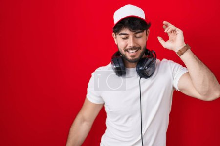 Photo for Hispanic man with beard wearing gamer hat and headphones dancing happy and cheerful, smiling moving casual and confident listening to music - Royalty Free Image