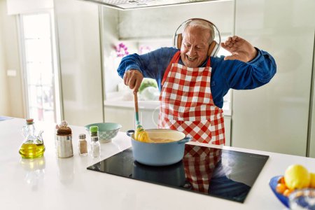Photo for Senior man listening to music cooking spaghetti at kitchen - Royalty Free Image