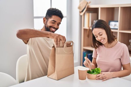Photo for Man and woman couple sitting on table eating take away food at home - Royalty Free Image