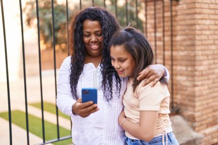 Foto de Madre e hija abrazándose entre sí usando un teléfono inteligente en la calle - Imagen libre de derechos