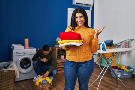 Foto de Young couple doing laundry at home smiling happy pointing with hand and finger to the side - Imagen libre de derechos