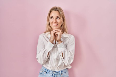 Téléchargez les photos : Jeune femme caucasienne portant une chemise blanche décontractée sur fond rose rire nerveux et excité avec les mains sur le menton regardant vers le côté - en image libre de droit