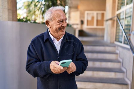 Foto de Hombre mayor sonriendo confiado usando teléfono inteligente en la calle - Imagen libre de derechos