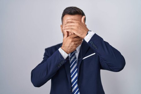 Photo for Handsome hispanic man wearing suit and tie covering eyes and mouth with hands, surprised and shocked. hiding emotion - Royalty Free Image