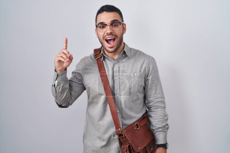 Photo for Young hispanic man wearing suitcase pointing finger up with successful idea. exited and happy. number one. - Royalty Free Image