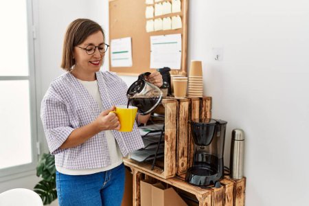 Foto de Mujer hispana de mediana edad mujer de negocios bebiendo una taza de café en la oficina de negocios - Imagen libre de derechos