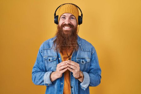Téléchargez les photos : Homme caucasien à longue barbe écoutant de la musique en utilisant les mains casque ensemble et les doigts croisés souriant détendu et joyeux. succès et optimisme - en image libre de droit