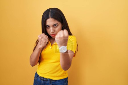 Photo for Young arab woman standing over yellow background ready to fight with fist defense gesture, angry and upset face, afraid of problem - Royalty Free Image