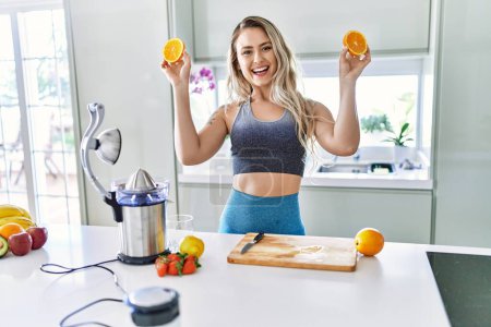 Foto de Mujer joven sonriendo confiada sosteniendo naranja en la cocina - Imagen libre de derechos