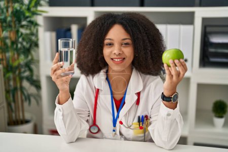 Téléchargez les photos : Young african american dietitian woman holding fresh apple and water winking looking at the camera with sexy expression, cheerful and happy face. - en image libre de droit