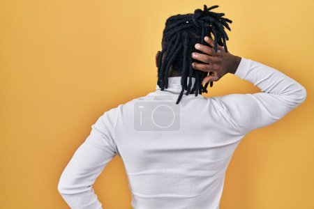 Foto de Hombre africano con rastas con jersey de cuello alto sobre fondo amarillo hacia atrás pensando en la duda con la mano en la cabeza - Imagen libre de derechos