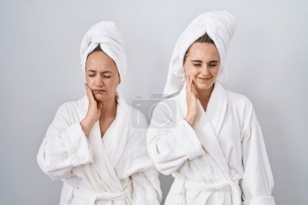 Téléchargez les photos : Middle age woman and daughter wearing white bathrobe and towel touching mouth with hand with painful expression because of toothache or dental illness on teeth. dentist - en image libre de droit