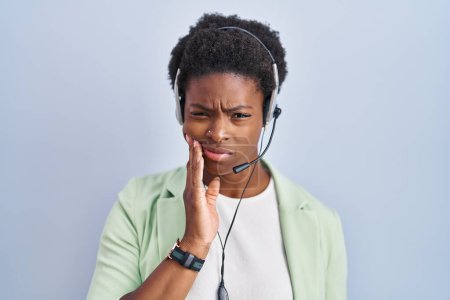 Foto de Mujer afroamericana que usa auriculares de agente de centro de llamadas tocando la boca con la mano con expresión dolorosa debido a dolor de muelas o enfermedad dental en los dientes. concepto de dentista. - Imagen libre de derechos