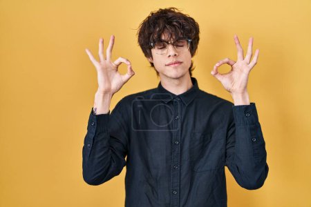 Photo for Young man wearing glasses over yellow background relax and smiling with eyes closed doing meditation gesture with fingers. yoga concept. - Royalty Free Image
