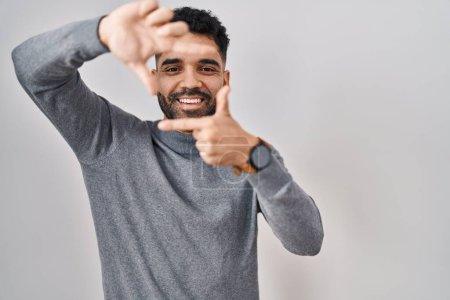 Téléchargez les photos : Homme hispanique avec barbe debout sur fond blanc souriant faisant cadre avec les mains et les doigts avec le visage heureux. concept de créativité et photographie. - en image libre de droit