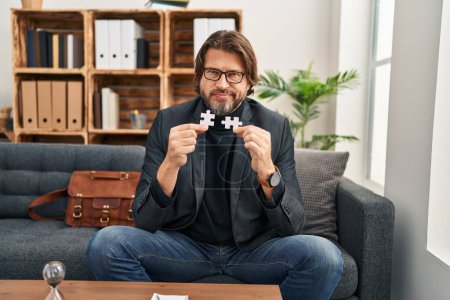 Photo for Handsome middle age man at consultation office holding puzzle pieces skeptic and nervous, frowning upset because of problem. negative person. - Royalty Free Image